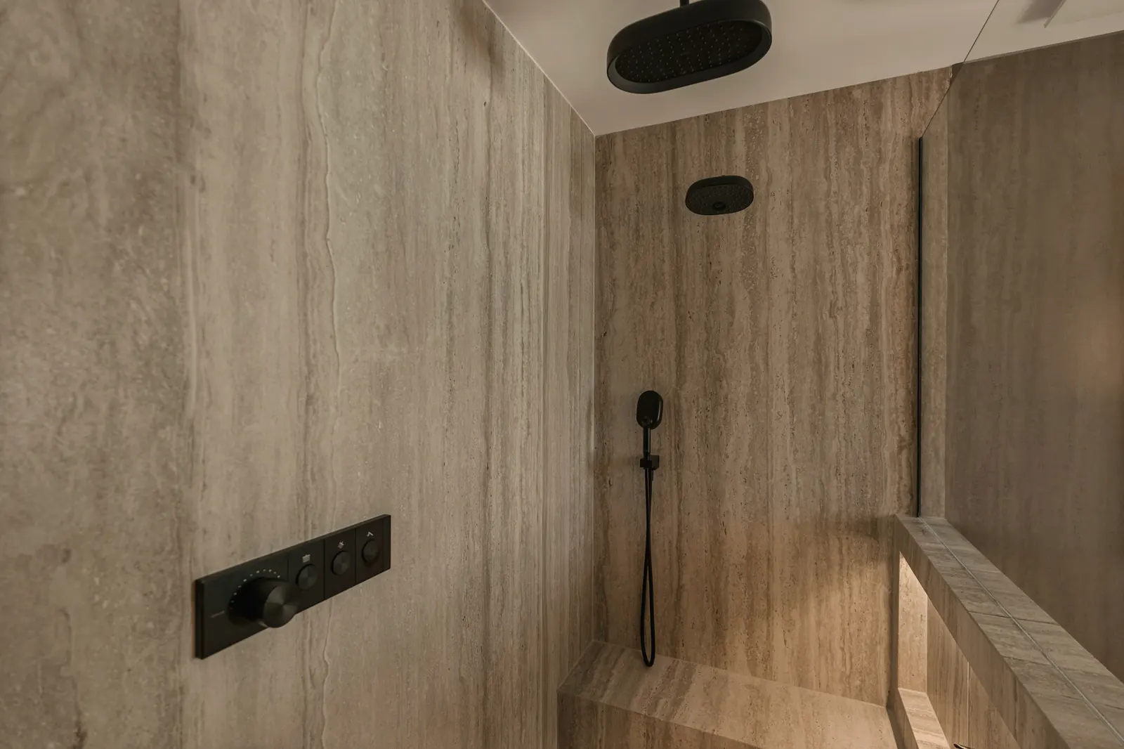 A walk-in shower in large-format stone tile with warm wood