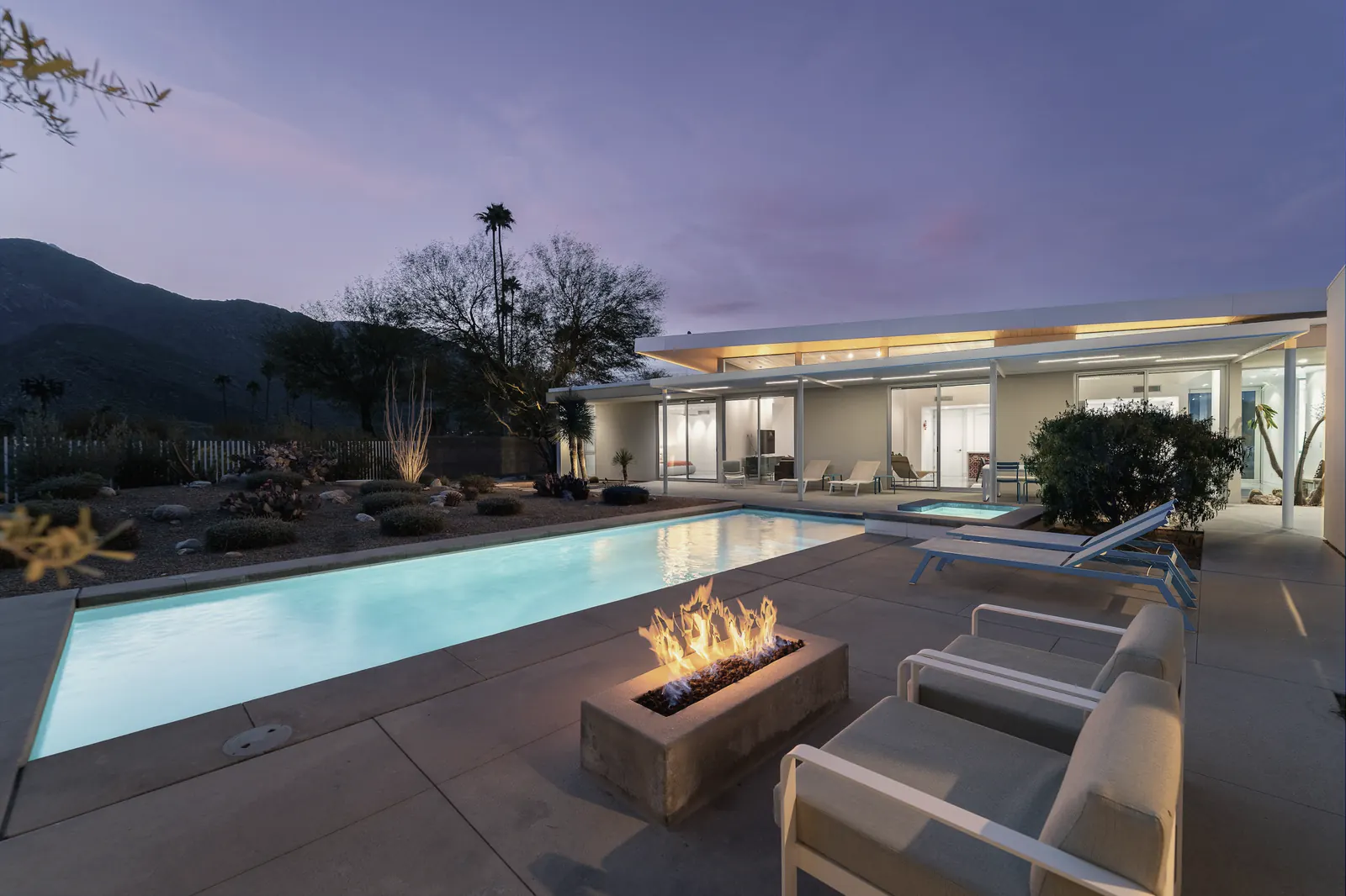 A fire table beside a pool on a desert patio at dusk